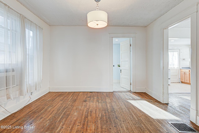 empty room featuring a textured ceiling, hardwood / wood-style floors, visible vents, and baseboards