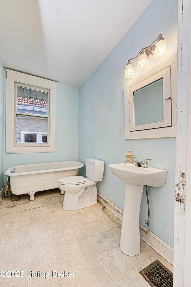 full bath with a freestanding bath, toilet, a sink, baseboards, and tile patterned floors