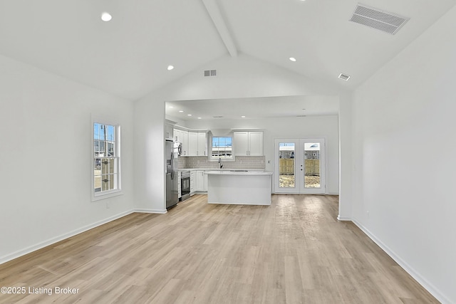 unfurnished living room with a sink, visible vents, baseboards, light wood-type flooring, and beam ceiling