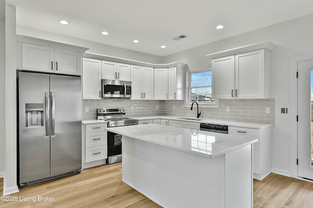 kitchen with stainless steel appliances, white cabinets, a sink, and a kitchen island