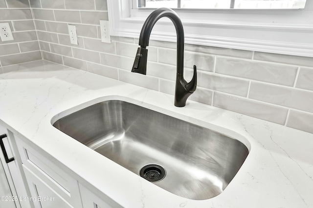 interior details featuring light stone countertops, tasteful backsplash, white cabinetry, and a sink