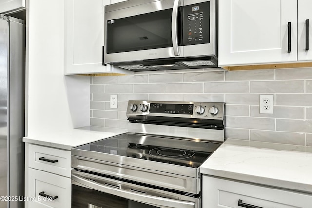 kitchen featuring appliances with stainless steel finishes, white cabinets, light stone counters, and tasteful backsplash