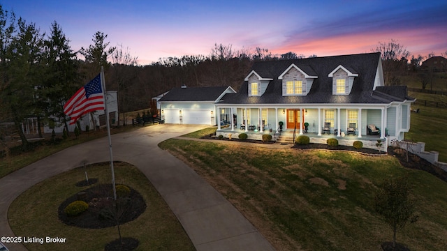 view of front facade with a porch, an attached garage, fence, concrete driveway, and a lawn