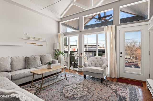 living area with plenty of natural light, high vaulted ceiling, ceiling fan, and dark wood-type flooring