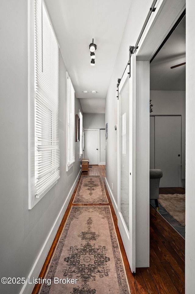 hallway featuring a barn door, baseboards, and dark wood-style flooring