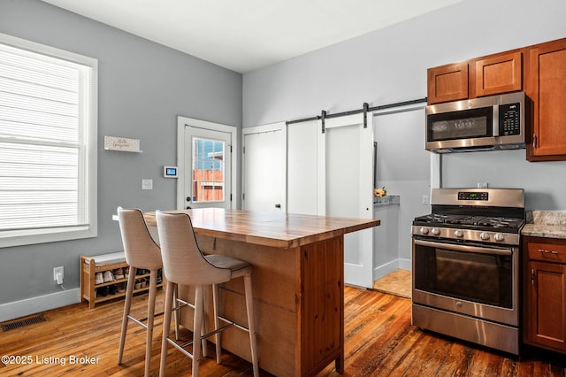 kitchen featuring a barn door, a breakfast bar, visible vents, appliances with stainless steel finishes, and brown cabinets