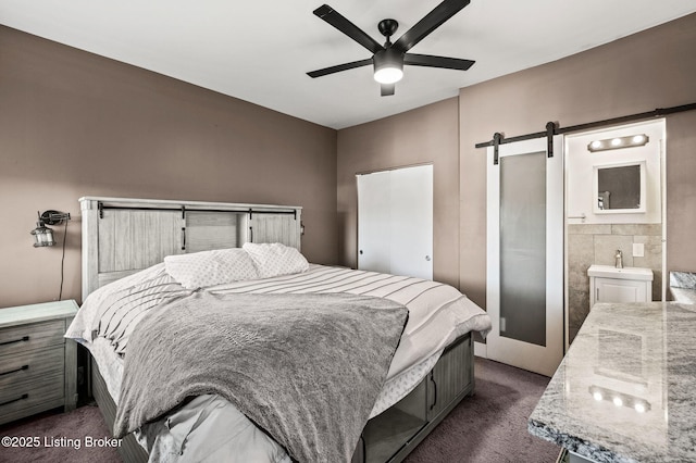 bedroom featuring dark colored carpet, a barn door, connected bathroom, and a ceiling fan