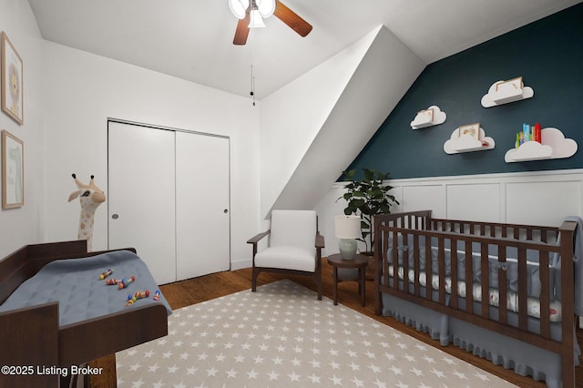 bedroom with a nursery area, a closet, a ceiling fan, vaulted ceiling, and light wood-type flooring