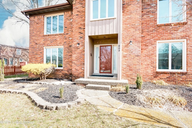 view of exterior entry with fence, board and batten siding, and brick siding