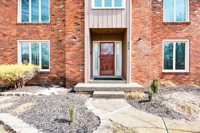 view of exterior entry featuring board and batten siding and brick siding