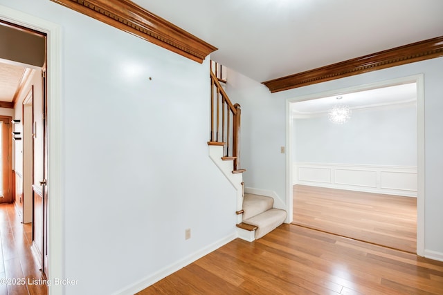 interior space with wainscoting, wood finished floors, stairs, crown molding, and a decorative wall