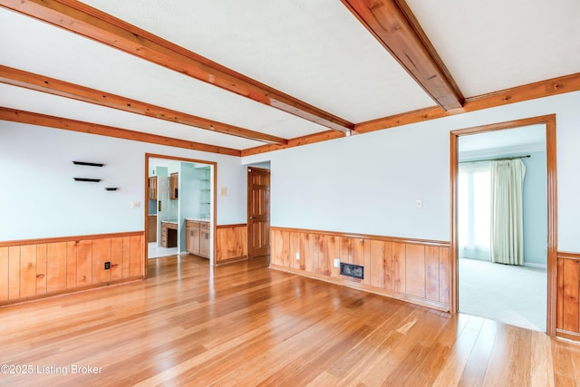 spare room featuring a wainscoted wall, light wood finished floors, and beam ceiling