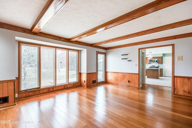 unfurnished living room featuring beam ceiling, a wainscoted wall, plenty of natural light, and a textured ceiling