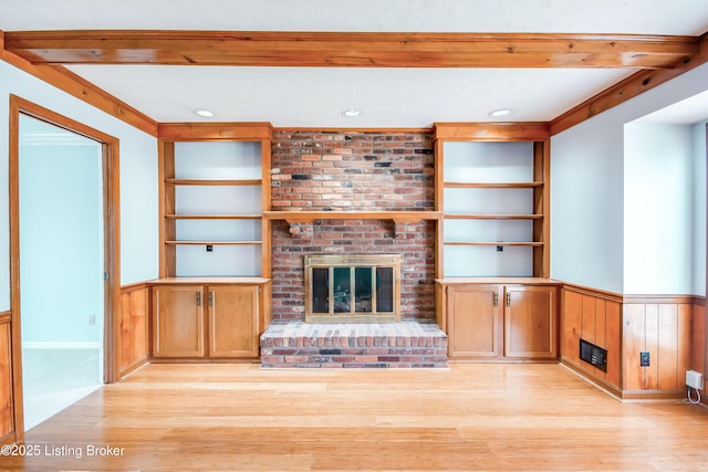 unfurnished living room featuring built in shelves, a brick fireplace, wainscoting, and light wood-style flooring