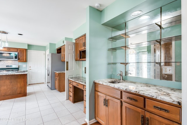 kitchen featuring light stone counters, a sink, appliances with stainless steel finishes, open shelves, and brown cabinetry