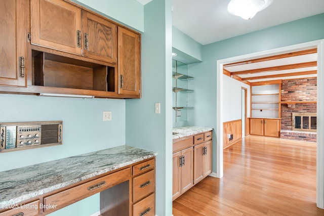 kitchen featuring light stone counters, light wood-type flooring, a brick fireplace, open shelves, and beamed ceiling