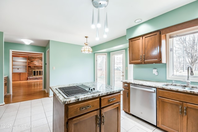 kitchen featuring brown cabinetry, appliances with stainless steel finishes, hanging light fixtures, a sink, and light tile patterned flooring