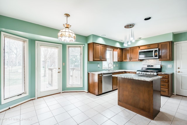 kitchen featuring a center island, decorative light fixtures, appliances with stainless steel finishes, brown cabinetry, and a sink