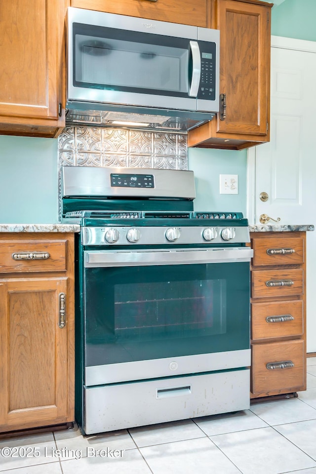 kitchen with light tile patterned floors, stainless steel appliances, light stone counters, and brown cabinetry