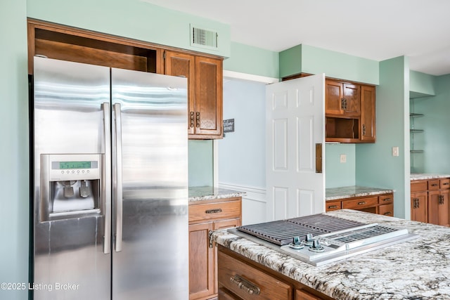 kitchen with visible vents, brown cabinetry, light stone counters, stainless steel appliances, and open shelves