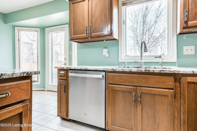 kitchen with light tile patterned floors, light stone counters, brown cabinets, stainless steel dishwasher, and a sink