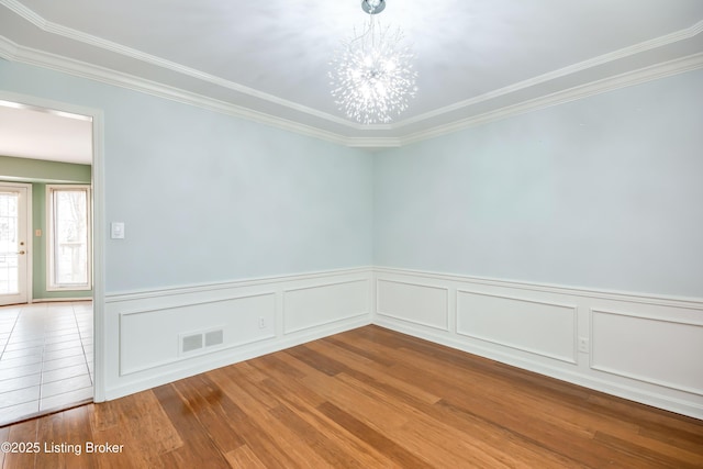 unfurnished room with a notable chandelier, wood finished floors, visible vents, wainscoting, and crown molding