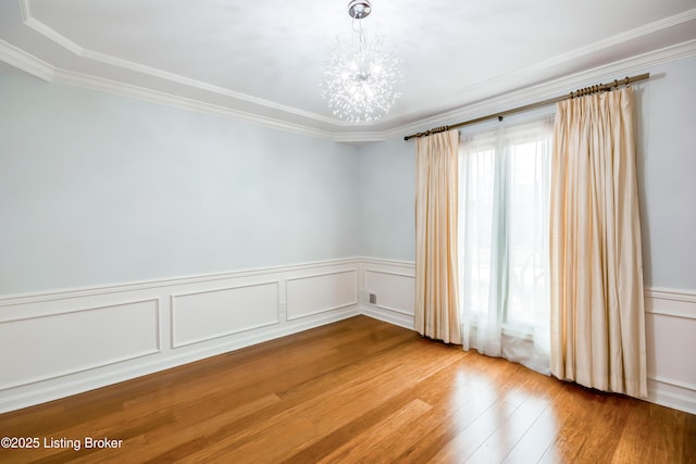 empty room featuring a wainscoted wall, ornamental molding, wood finished floors, and an inviting chandelier