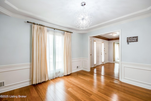 unfurnished room with a wainscoted wall, a chandelier, wood finished floors, and ornamental molding