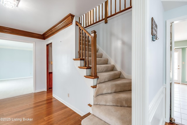 stairway with crown molding, visible vents, baseboards, and wood finished floors