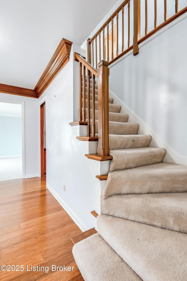 staircase featuring crown molding, baseboards, and wood finished floors