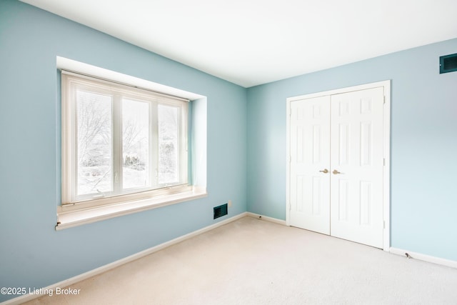 unfurnished bedroom featuring a closet, light carpet, visible vents, and baseboards