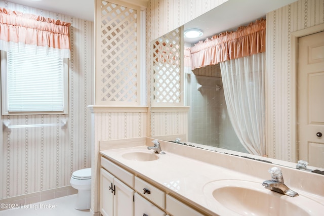 bathroom with double vanity, a sink, toilet, and wallpapered walls