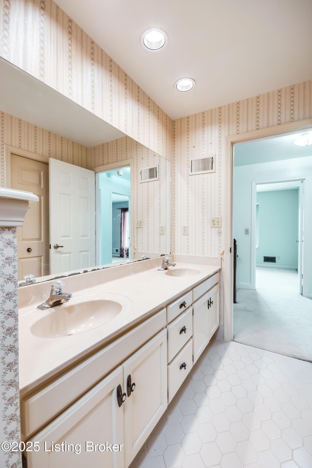 bathroom with double vanity, visible vents, a sink, and wallpapered walls