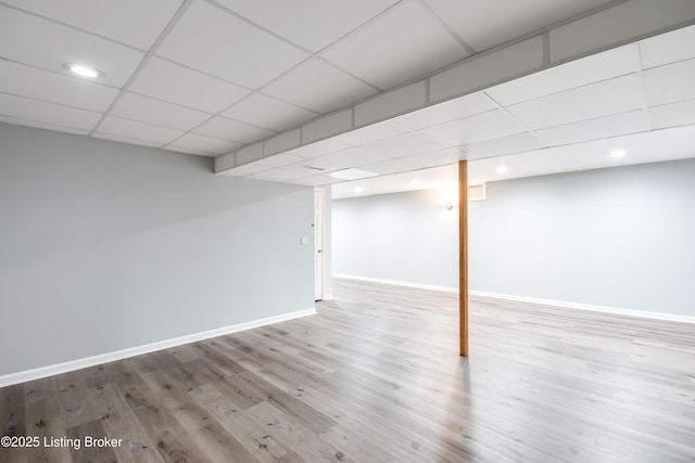 finished basement featuring a paneled ceiling, baseboards, and wood finished floors