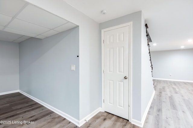 corridor featuring light wood-type flooring, baseboards, and a drop ceiling