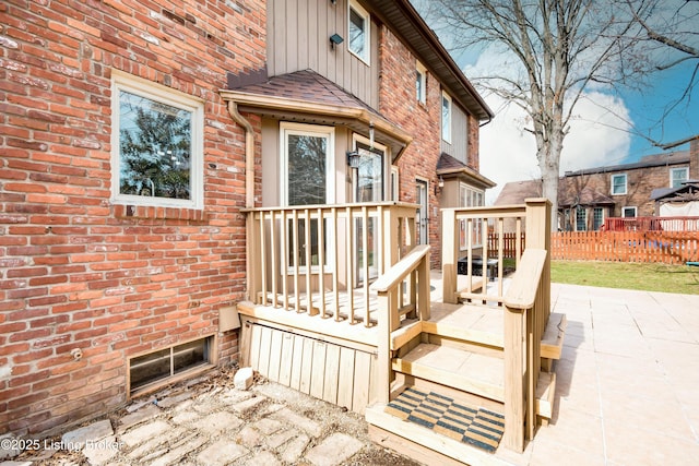 view of exterior entry with brick siding, a shingled roof, board and batten siding, a patio area, and fence