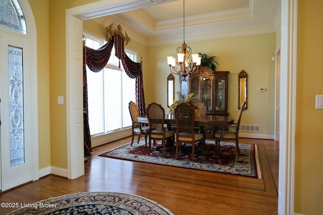 dining room featuring a tray ceiling, a chandelier, wood finished floors, and ornamental molding