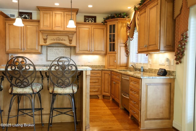 kitchen with light wood finished floors, glass insert cabinets, light stone countertops, a kitchen bar, and a sink