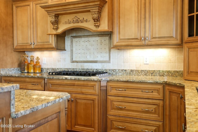 kitchen featuring tasteful backsplash, custom range hood, glass insert cabinets, light stone counters, and stainless steel gas cooktop