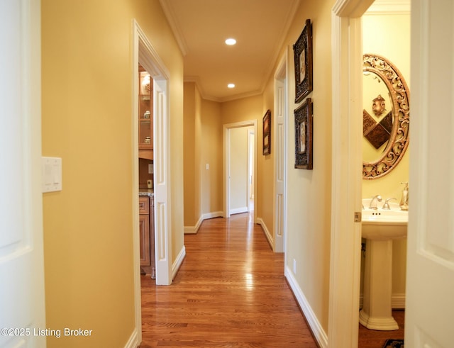 hall with recessed lighting, a sink, baseboards, light wood-type flooring, and crown molding