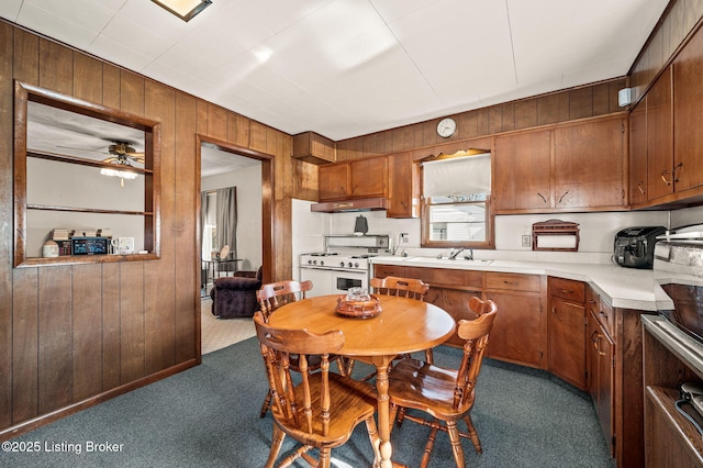 kitchen featuring brown cabinets, light countertops, white gas stove, under cabinet range hood, and dark carpet