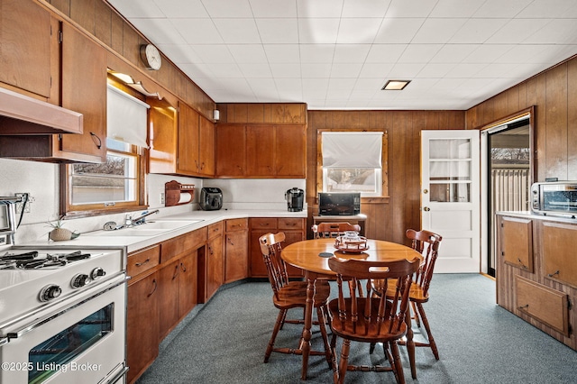 kitchen featuring white gas stove, wood walls, light countertops, and brown cabinets