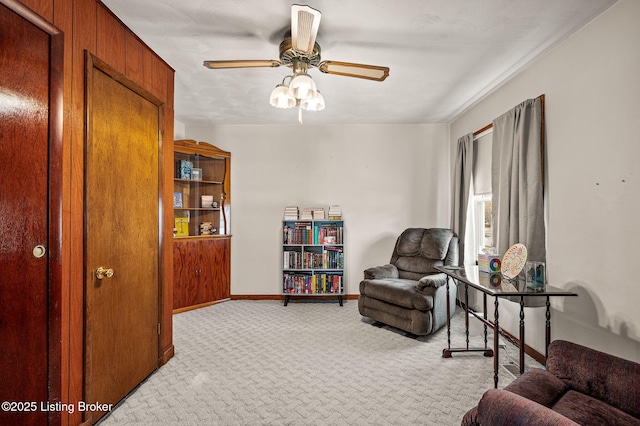 living area featuring a ceiling fan, light colored carpet, and baseboards