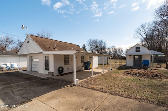 view of front of home featuring driveway, roof with shingles, an outdoor structure, and fence