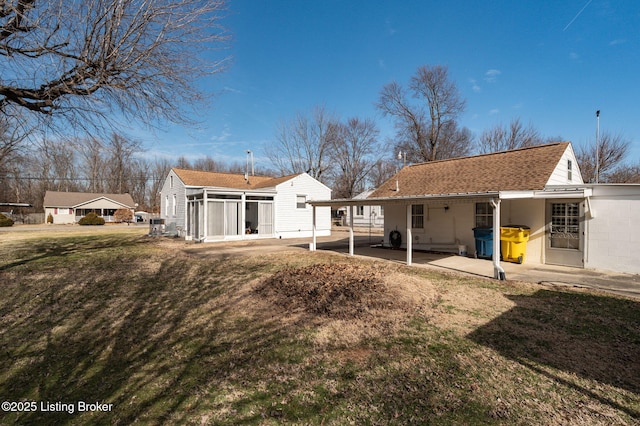 rear view of house featuring a yard, a shingled roof, and a sunroom