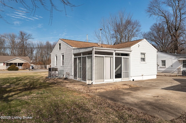 rear view of property featuring a shingled roof, a sunroom, central AC, and a lawn