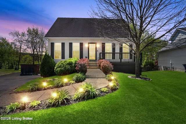 cape cod-style house featuring covered porch, a shingled roof, aphalt driveway, and a lawn