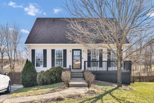 new england style home with a shingled roof, fence, and a front yard