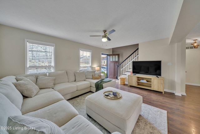 living room with ceiling fan, a textured ceiling, wood finished floors, baseboards, and stairs