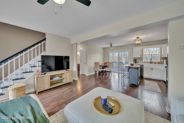 living room with dark wood-style flooring, ceiling fan, baseboards, and stairs